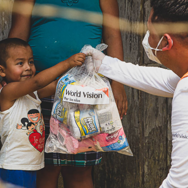 World Vision Mitarbeiter überreicht Gesundheitspaket an ein lächelndes Kind